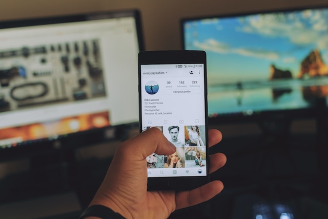 黒いスマートフォンを持つ手の写真。Instagram のプロフィールページが表示されている。