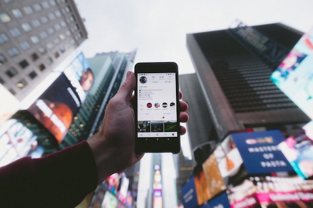 Photo d'une personne tenant un téléphone et montrant le profil d'un utilisateur de Instagram avec un contenu visuel et des points forts.