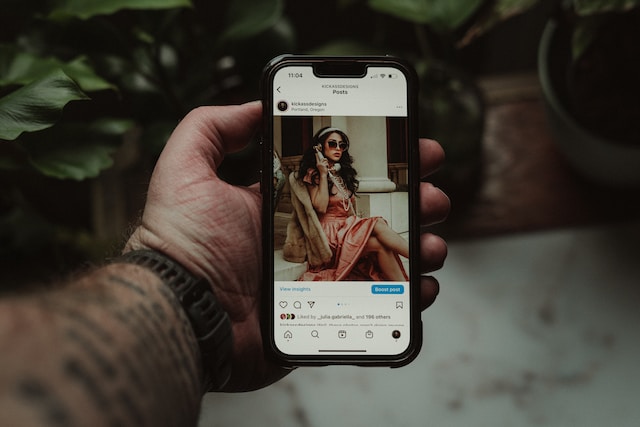 A picture of a hand holding a smartphone displaying an Instagram post of a woman.