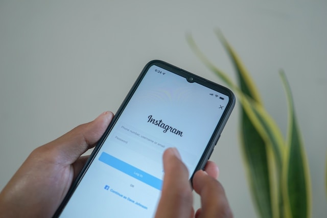 A picture of a hand holding a black smartphone displaying the Instagram app sign-in page.