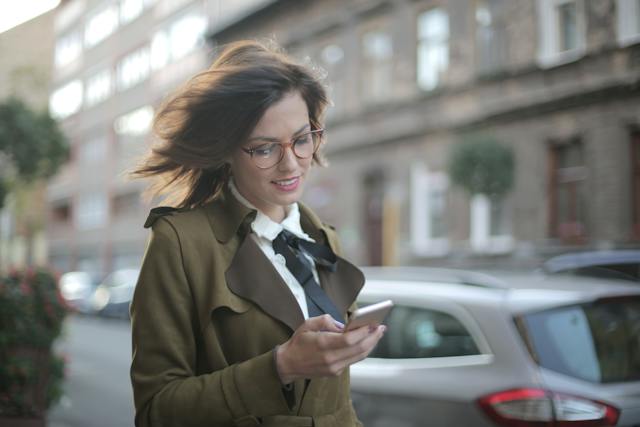 Eine Frau geht die Straße entlang und schaut auf eine Nachricht auf ihrem Handy.