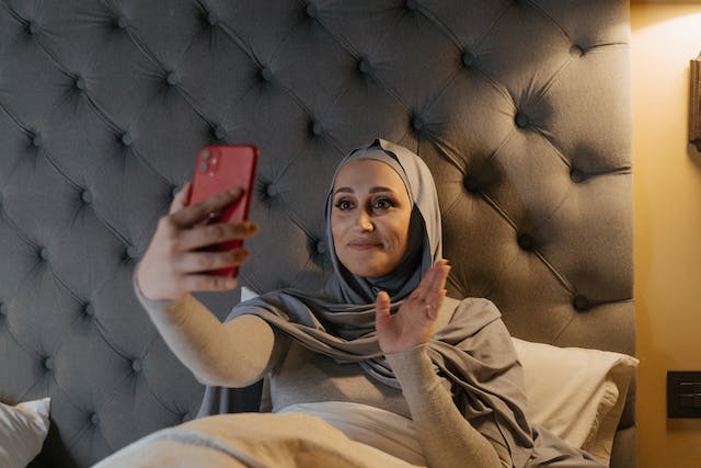 Woman in hijab waving at red iPhone while recording an Instagram Live video.