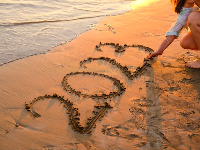 A girl writing “2023” in the sand with her fingers to bid the year goodbye.