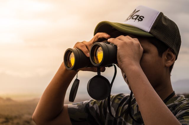 Un uomo osserva segretamente qualcuno da lontano utilizzando un binocolo.