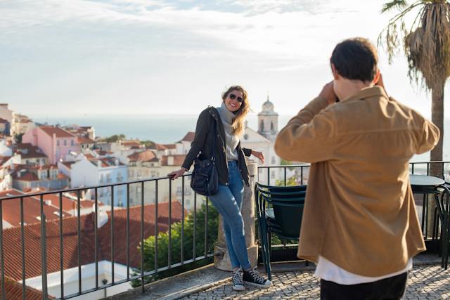 A man taking a photo of a woman during one of their travels as a couple.