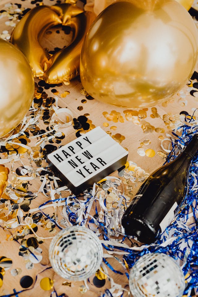 A sign that says “Happy New Year” with confetti, balloons, party décor and wine glasses on the floor.