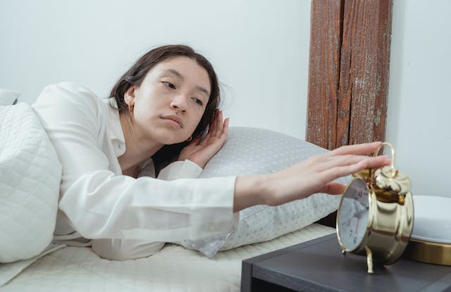Una empresaria que pulsa el botón de repetición de su despertador para volver a dormir después de automatizar las tareas en línea.