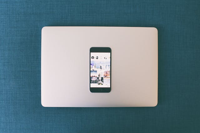 Un telefon se sprijină pe un laptop, afișând o grilă foto dintr-un Instagram profil.