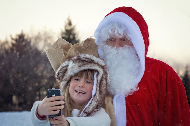 O fetiță care își face un selfie cu Moș Crăciun.