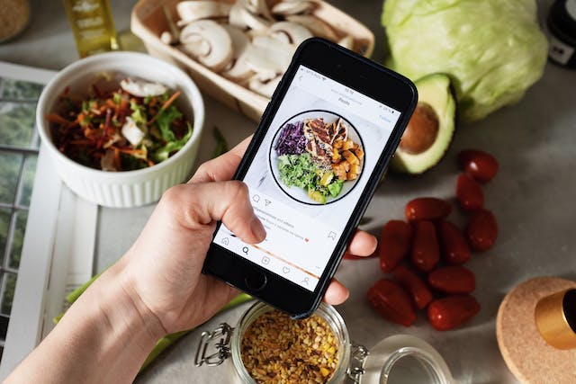 A picture of a hand holding a black smartphone displaying an Instagram post about food.