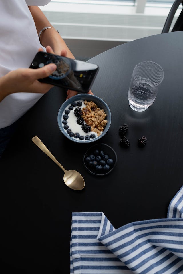 O bloggeriță culinară de pe Instagram fotografiază mâncarea din fața ei pentru a o încărca online.
