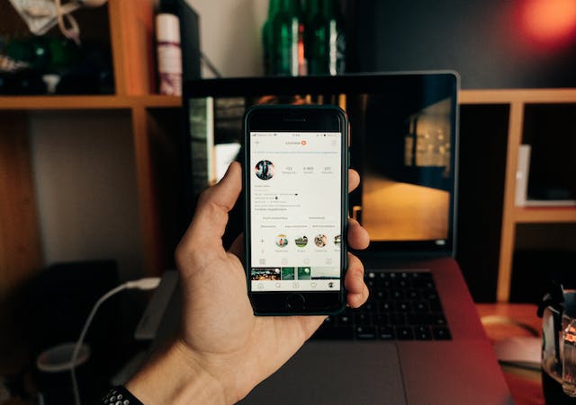 A person holds a phone with an Instagram profile on the screen.