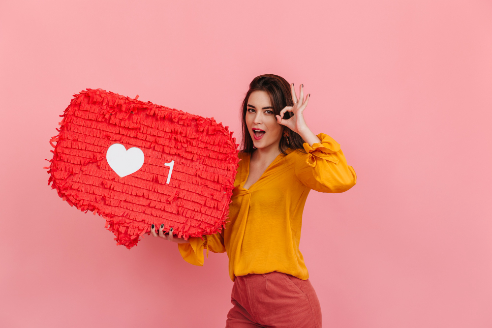 A girl in a yellow shirt holding a pinata shaped like an Instagram heart sign.