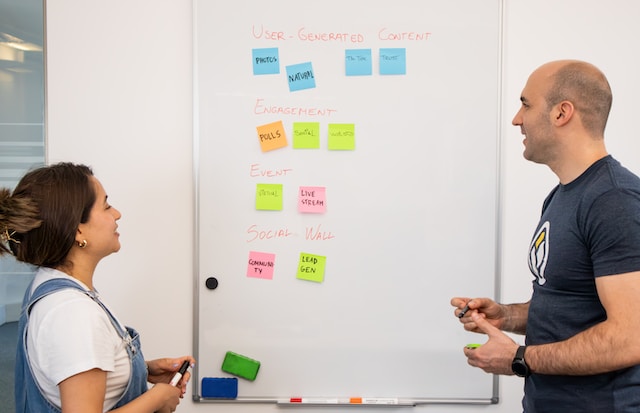 Two people stand in front of a whiteboard planning user-generated content.