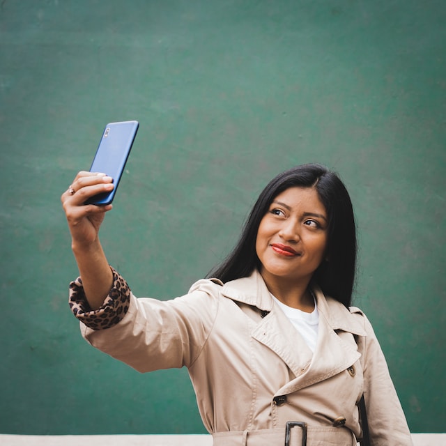 Een vrouw in een blauwe jas die een selfie met haar telefoon neemt om op hun te posten Instagram rekening.