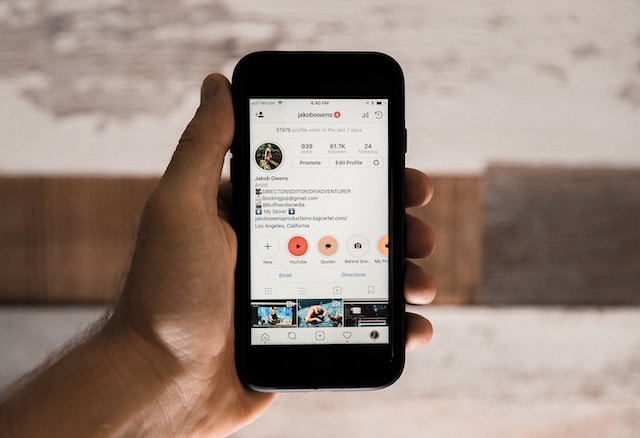 Uma imagem de uma mão a segurar um smartphone preto que apresenta uma página de perfil Instagram .