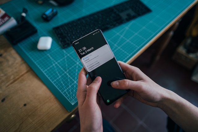 A person holding a smartphone with a keyboard and iPods in the background.