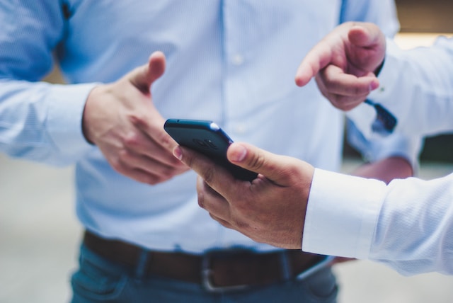 Un homme en chemise bleue montrant son téléphone. 