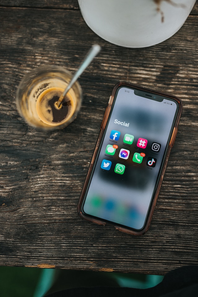 An Android phone with social media apps on the screen is placed on a wooden table beside a coffee glass.