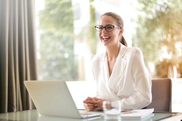 Una empresaria con traje blanco y gafas delante de su portátil en una oficina.