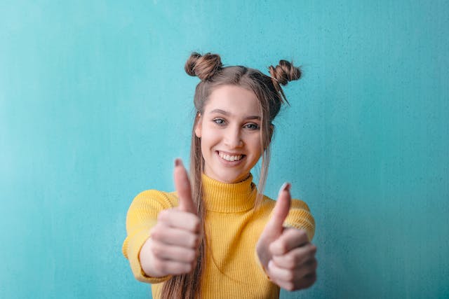 A woman smiling and holding her two thumbs up.