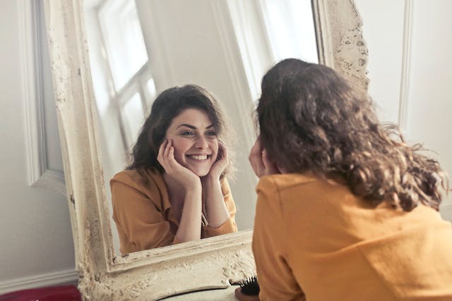 A happy, confident woman smiling while looking at herself in the mirror.