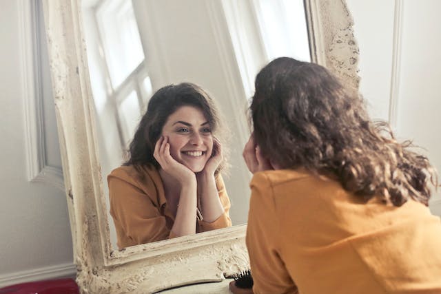 Een gelukkige, zelfverzekerde vrouw die glimlacht terwijl ze zichzelf in de spiegel bekijkt.