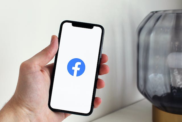 A person holding up an iPhone displaying the Facebook logo.