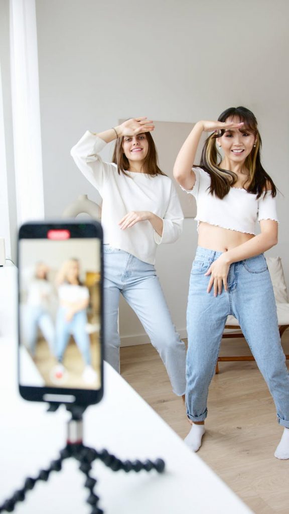 Due donne in top bianco e jeans denim ballano e registrano un video.