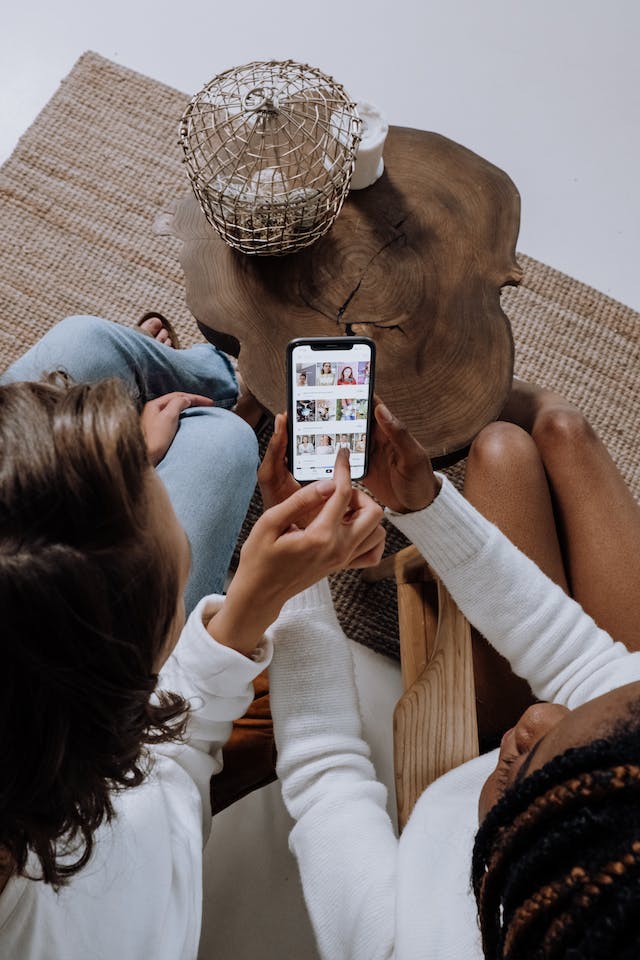 Two women scrolling through a social media app on a smartphone.