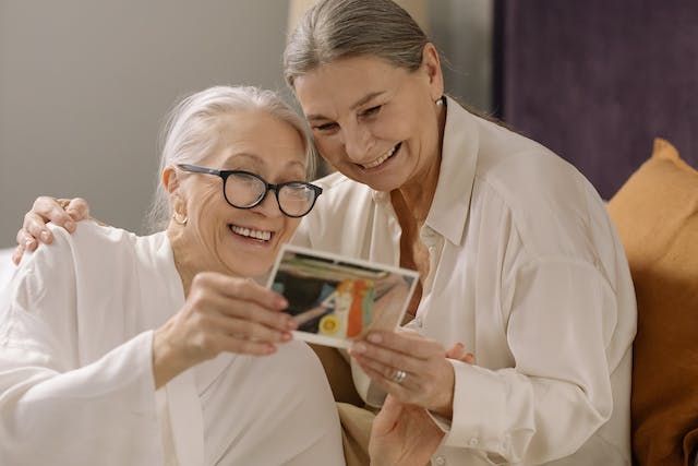 Two elderly women smiling while looking at an old photograph together.