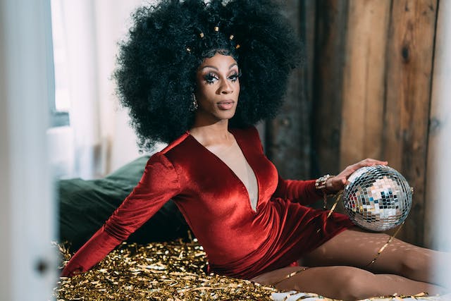 Drag queen with a red dress and afro holding a sparkling disco ball.