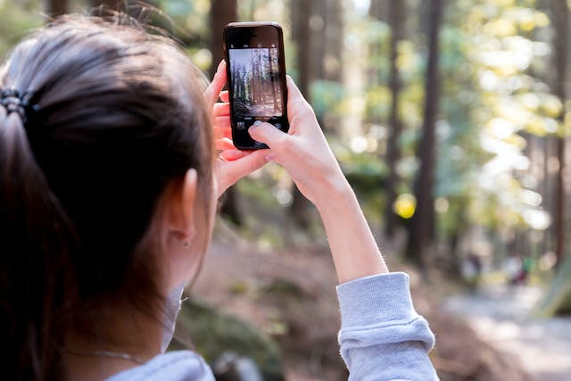 A female content creator is taking a picture of the forest for her Instagram account. 