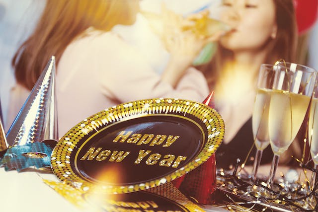 Party supplies on a table, including party hats, drinks, and gold plates that say “Happy New Year!”