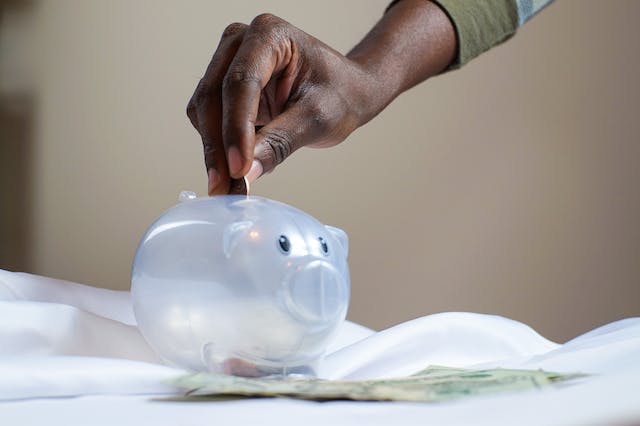 Someone putting a coin into a transparent piggy bank.