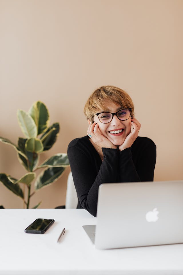 Uma mulher sorridente sentada numa mesa com o seu computador portátil enquanto vê o seu filme repostado em Instagram.