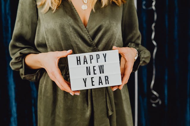 Une femme vêtue d'une robe de soirée vert olive brandit un tableau d'affichage sur lequel est écrit "Bonne année".