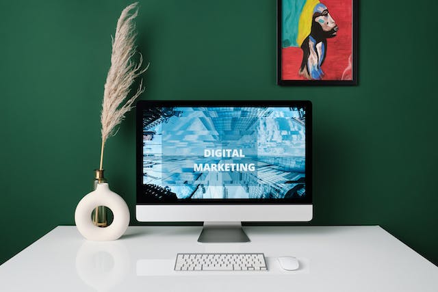 A work desk with a computer screen with the words “Digital Marketing” on it.