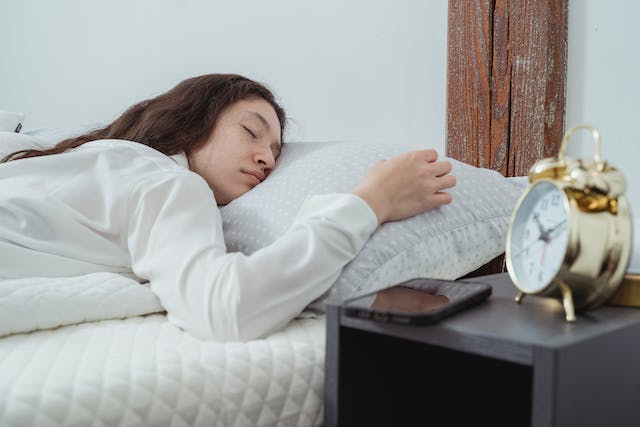 A woman sleeping in bed in a comfortable, face-down position while ignoring her alarm clock.