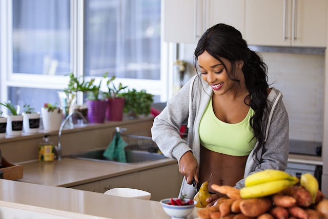 Een vrouw in trainingskleren snijdt kalebassen in de keuken om een gezonde maaltijd in elkaar te flansen.