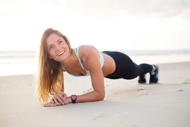 A smiling female fitness trainer doing a plank on the beach.