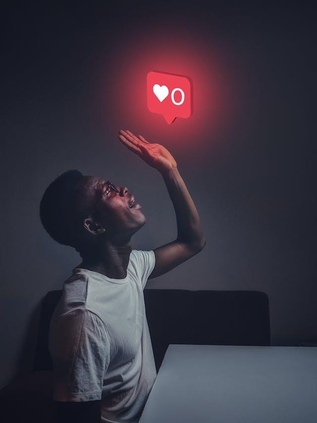 A man looking up at a neon symbol of an Instagram “like” heart. 