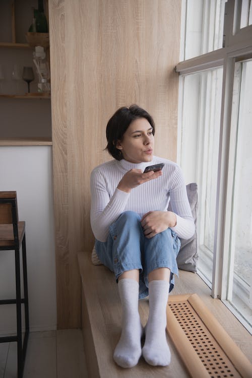 Une femme assise à côté d'une fenêtre tout en envoyant une note vocale sur Instagram.