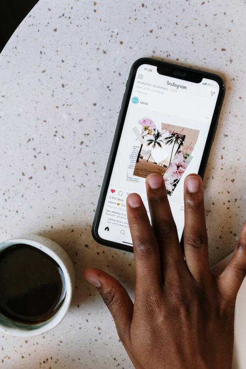 Una persona che apprezza una foto di Instagram sul proprio cellulare accanto a una tazza di caffè.