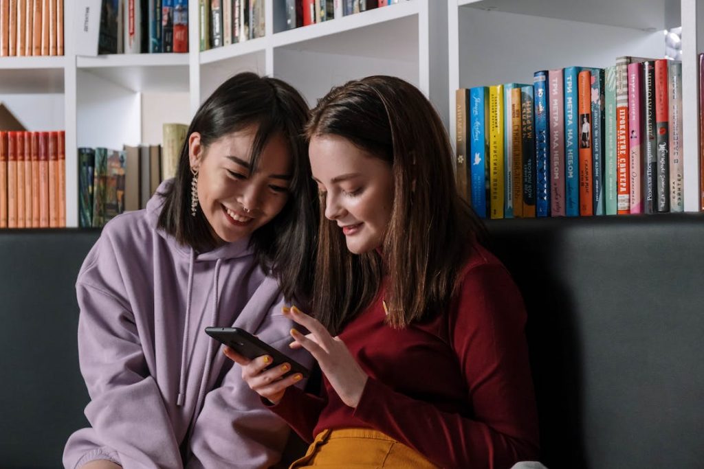 Two teenage girls happily use social media on a smartphone.