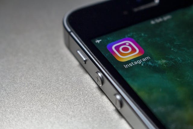 Uma imagem de um grande plano do logótipo da aplicação Instagram apresentado no ecrã de um smartphone preto.