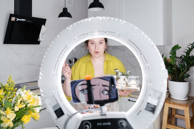 An influencer recording a video in the kitchen with their phone camera and tripod.