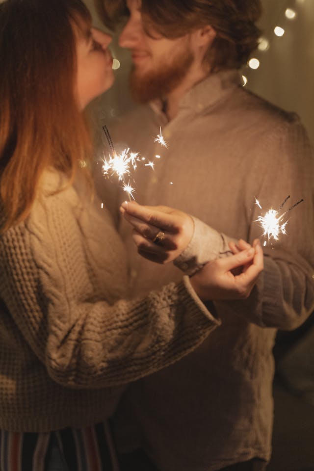 Una coppia con le stelle filanti in mano sta per scambiarsi un bacio di Capodanno a mezzanotte