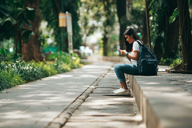 공원 벤치에 앉아 Instagram 에서 차단된 사용자 목록을 보고 있는 한 소녀 .