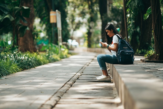 A girl sitting on a park bench looking at her blocked users list on Instagram.